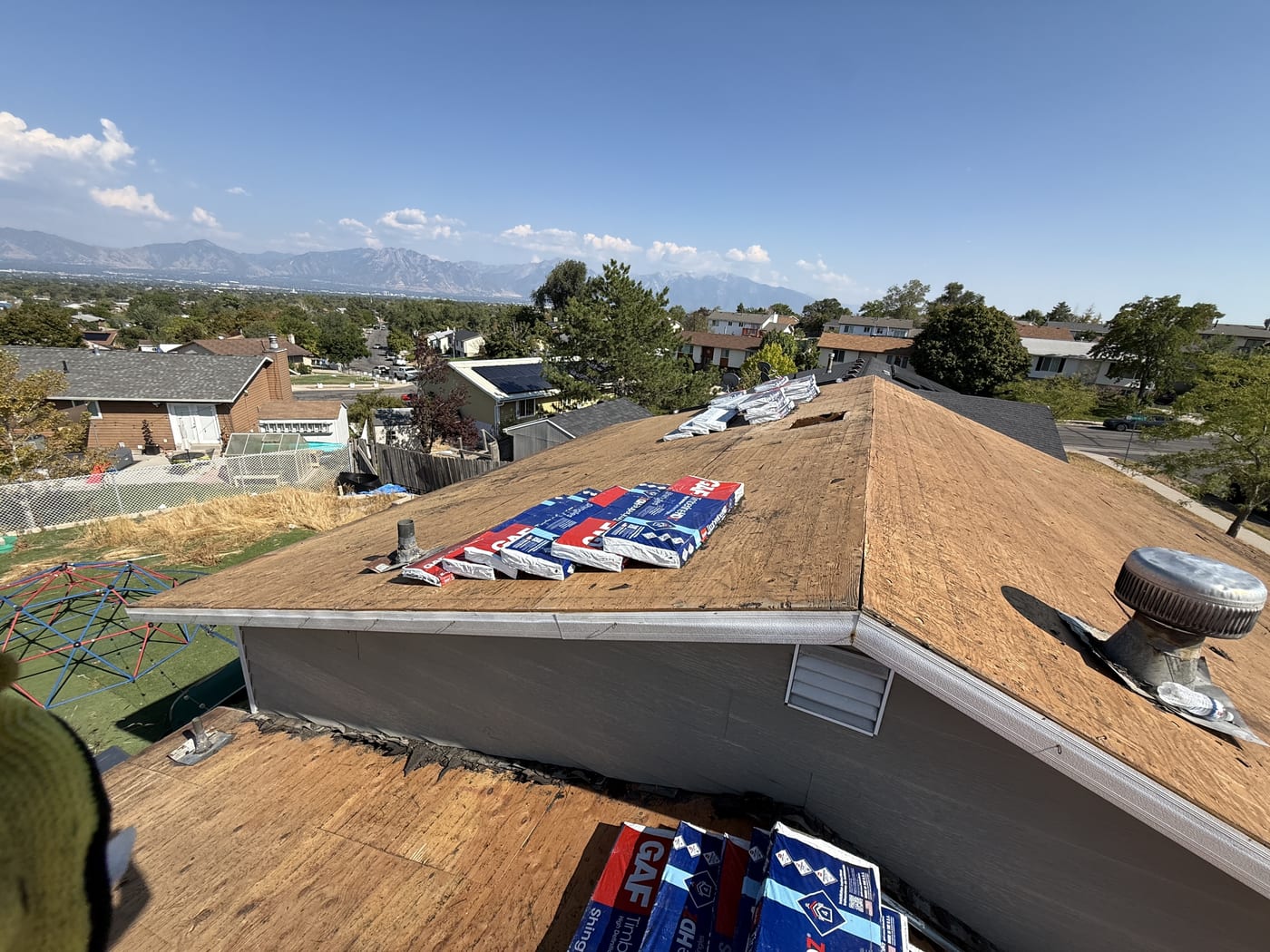 View from roof showing bare OSB deck with roofing supplies and neighborhood, in-progress re-roof phase
