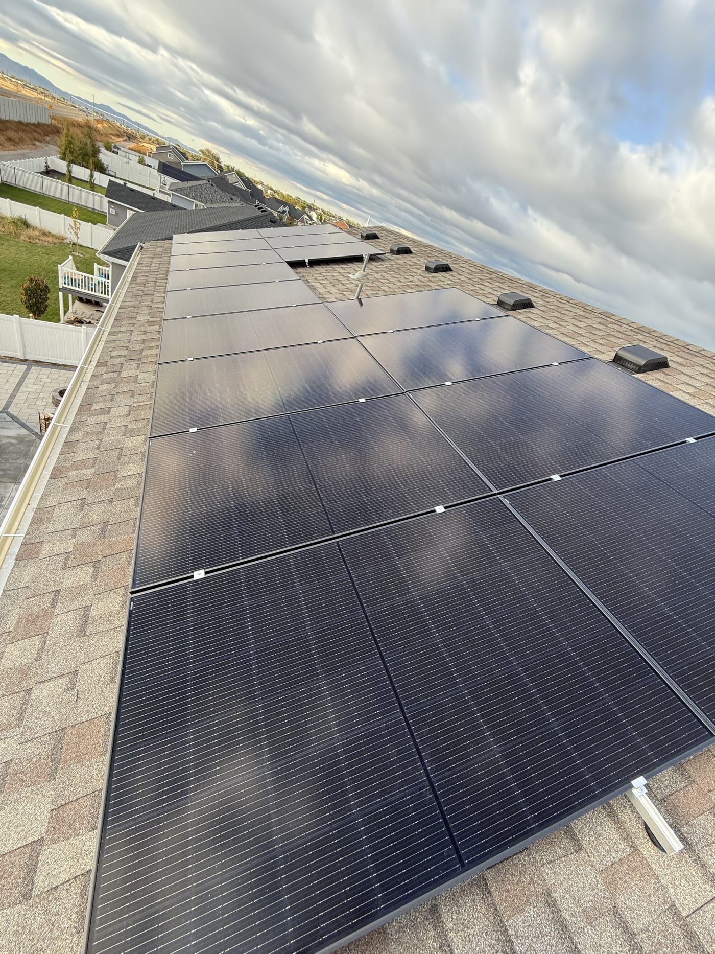 [Trina panels] Close-up of solar panels on shingle roof with racking hardware, cloudy sky and house exterior visible