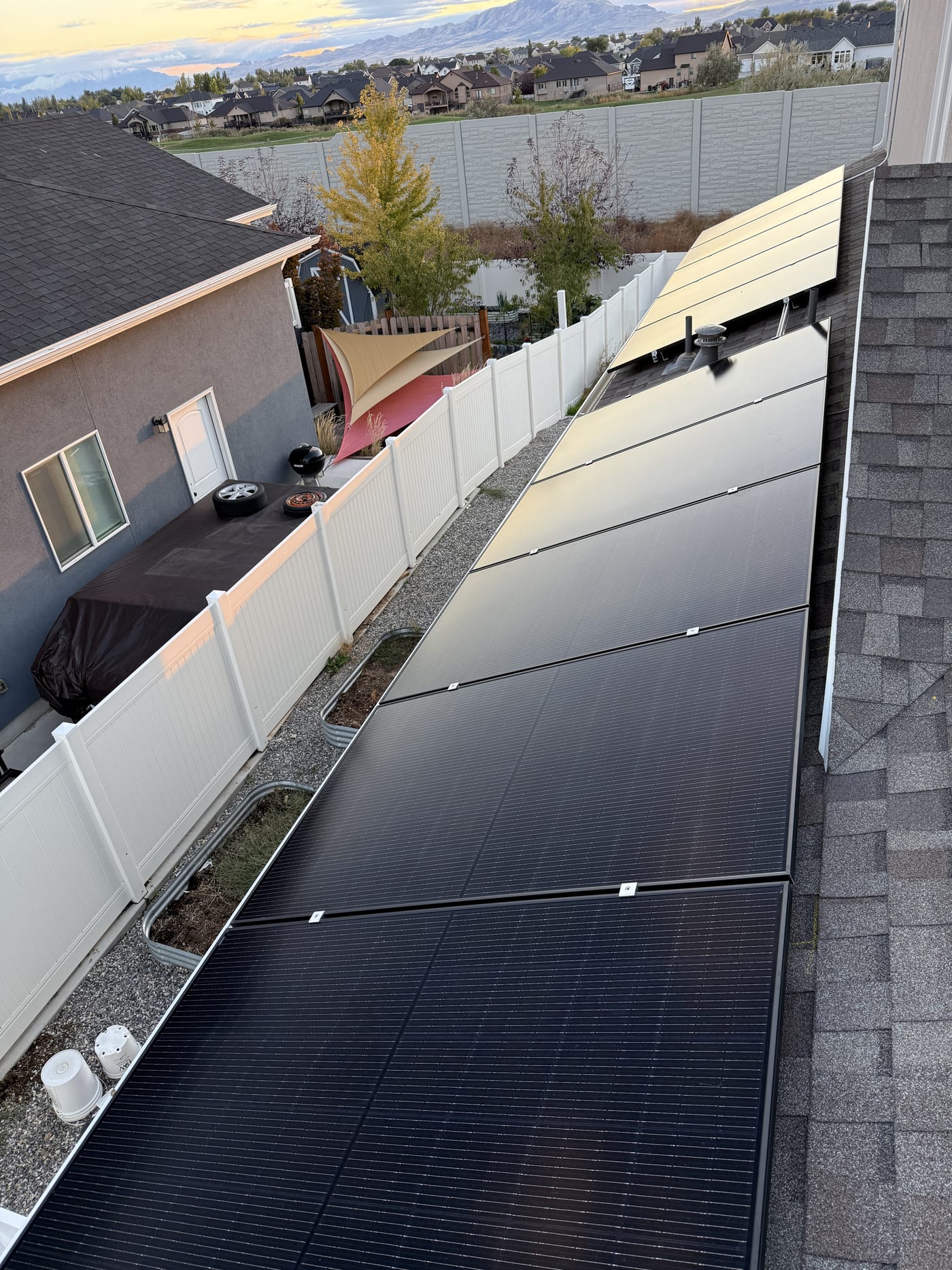 [Trina panels] Close-up of solar panels on roof at golden hour/dusk, house patio and property visible below, warm sunset lighting