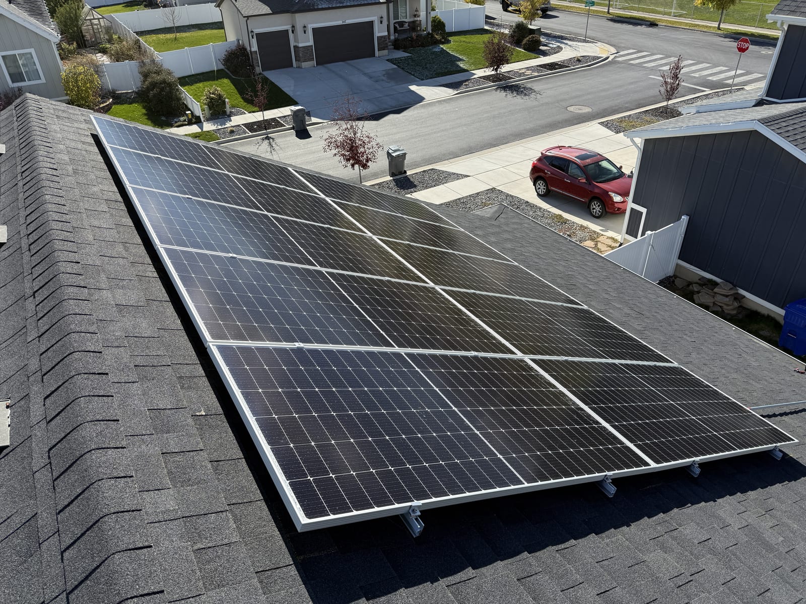 Drone overhead view of full solar panel array on residential rooftop with driveway, car, and neighborhood visible below
