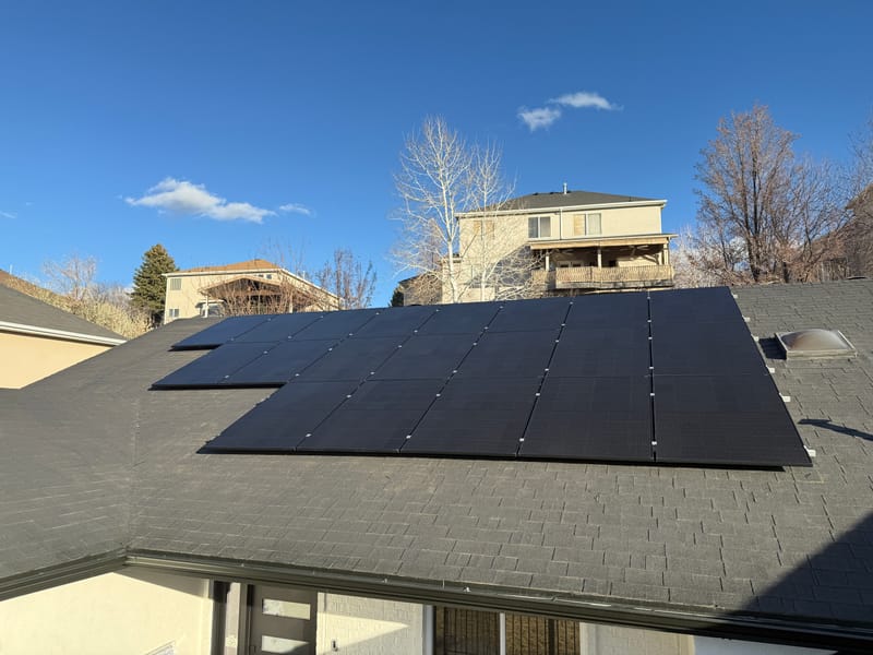 [black-on-black Trina panels] Scenic rooftop solar installation with mountain backdrop and clear weather conditions.