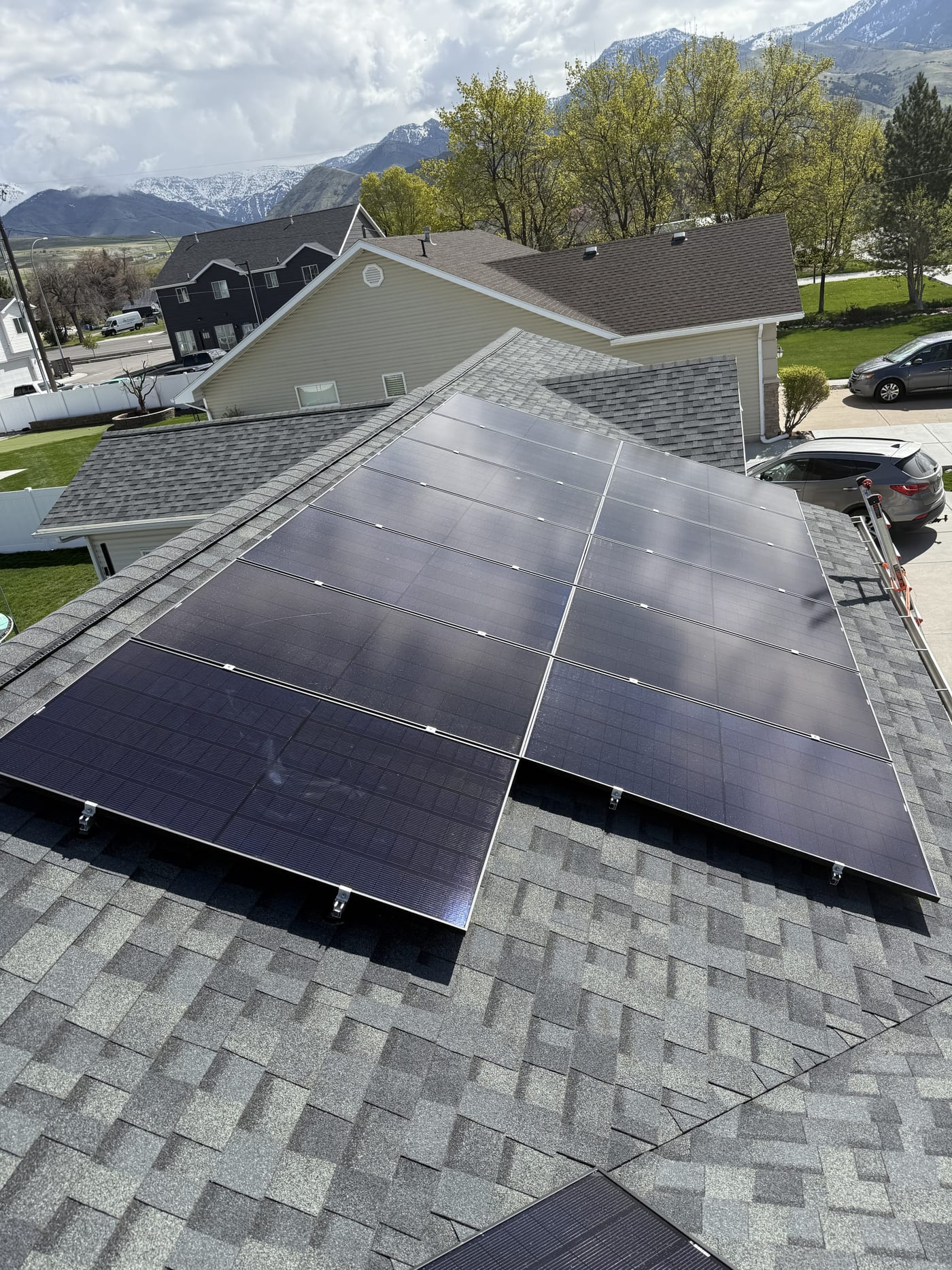 [black-on-black panels] Solar array on shingle roof from elevated angle with neighborhood visible