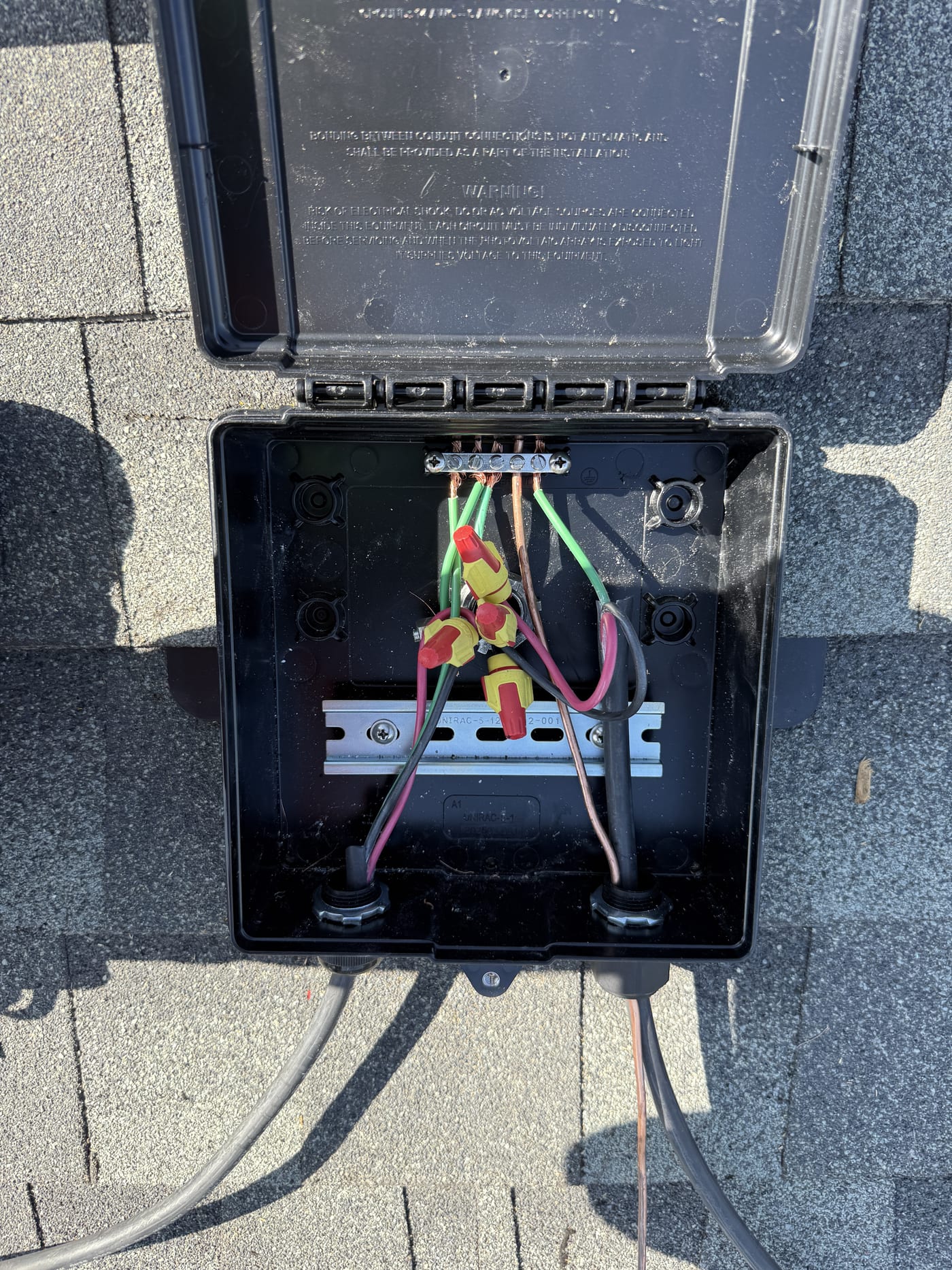 Open junction box on shingle roof showing wire connections
