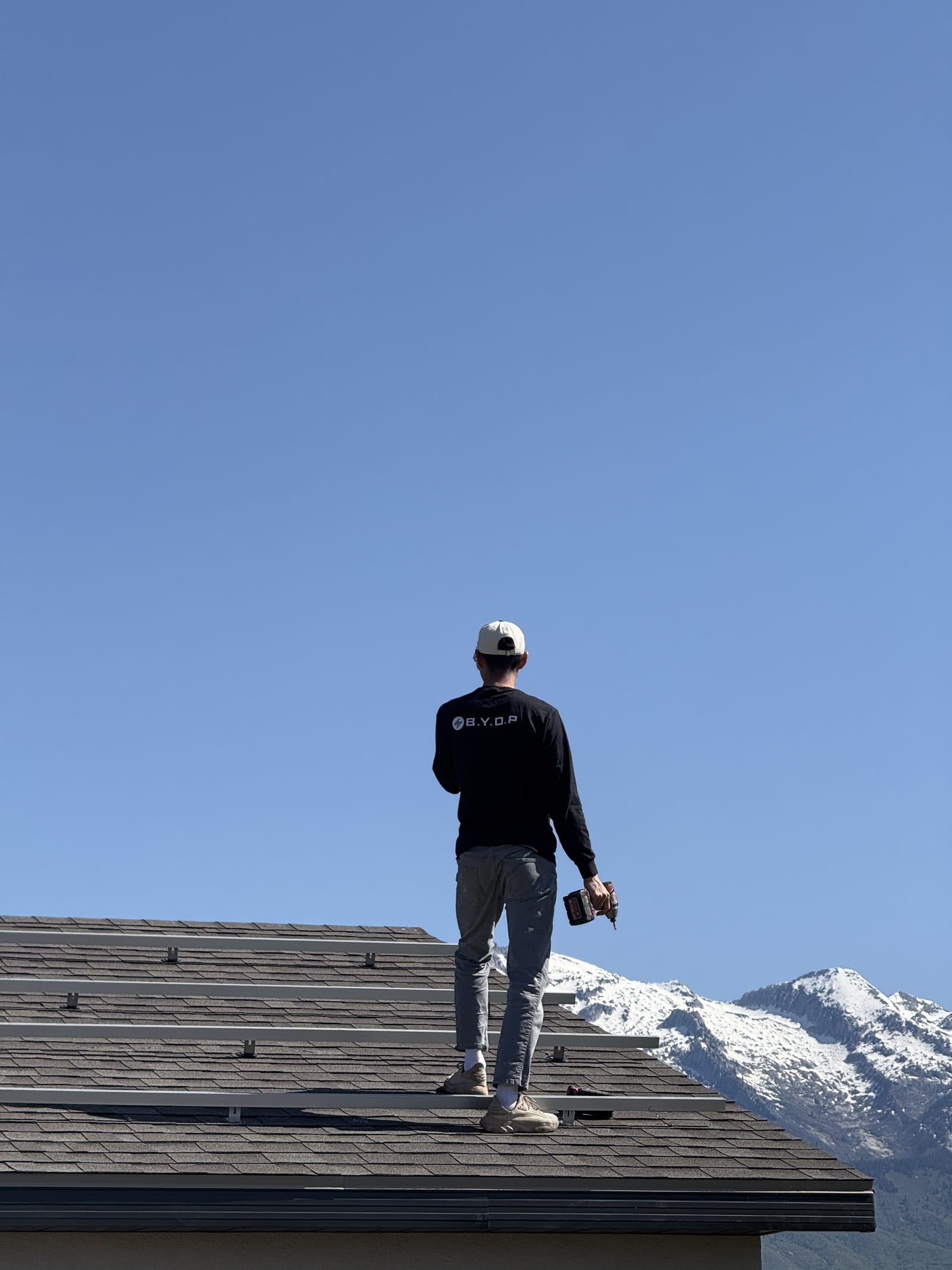 BYOP crew member on roof with snow-capped mountains in background during solar installation