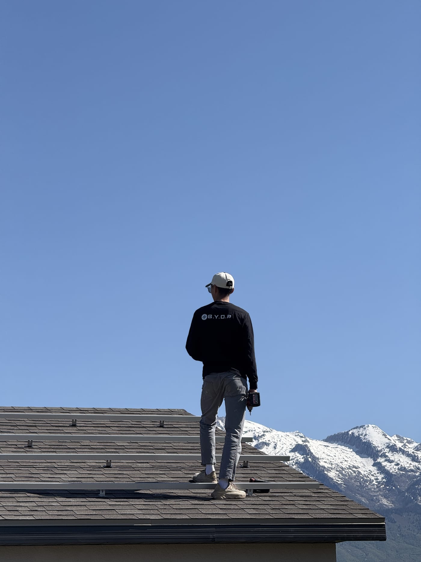 BYOP installer on roof with solar panels and snow-capped Utah mountains in background