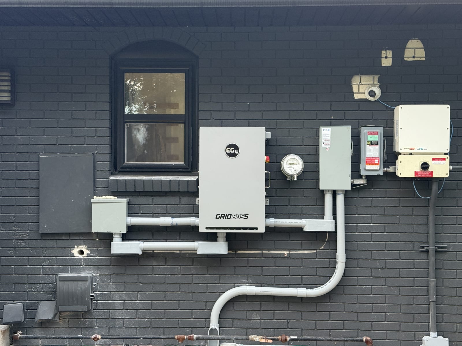 Clean EG4 GridBOSS inverter installation with meter disconnect and conduit on dark brick exterior wall