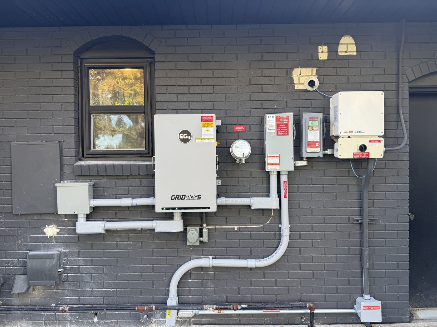 EG4 GridBOSS inverter with meter disconnect and warning labels on dark brick wall