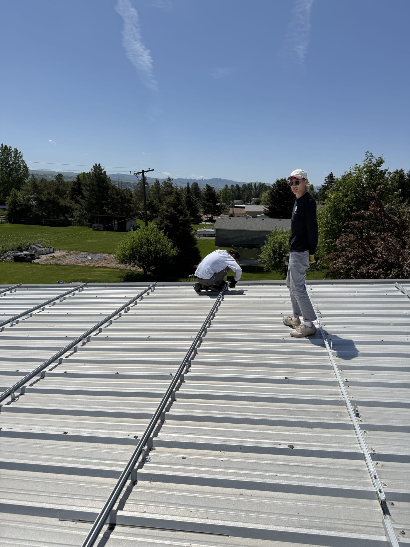 Two crew members on metal standing seam roof with ladder during racking installation on rural property