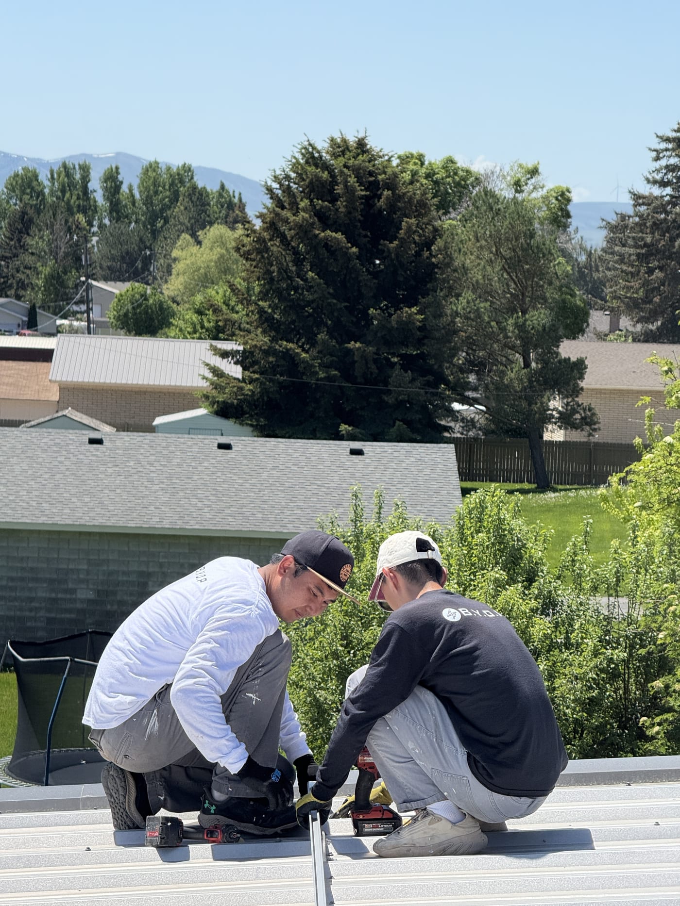 Two crew members on metal roof edge with neighborhood and trees in background