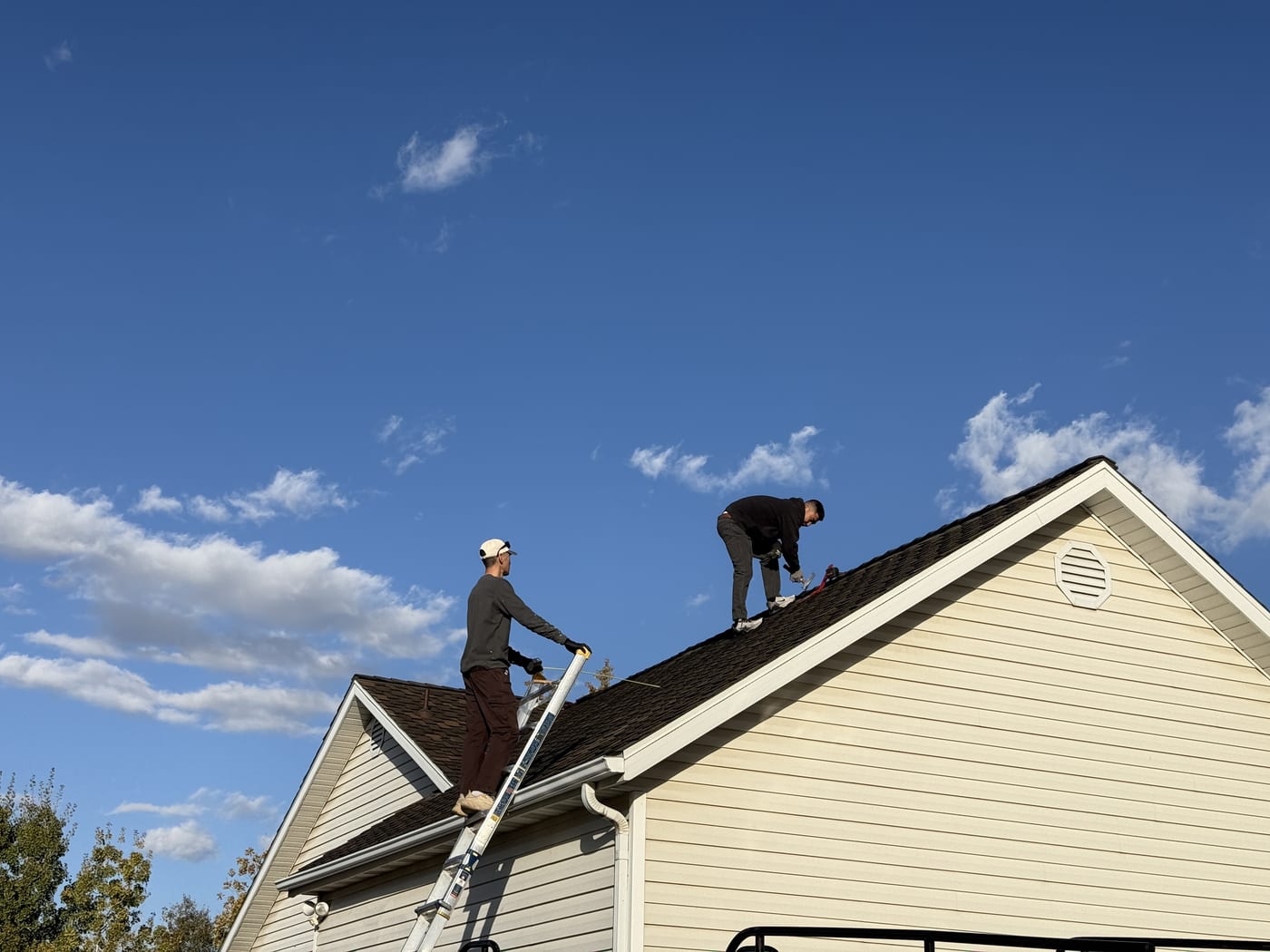 Two crew members on ladder at house roofline with blue sky during solar installation setup