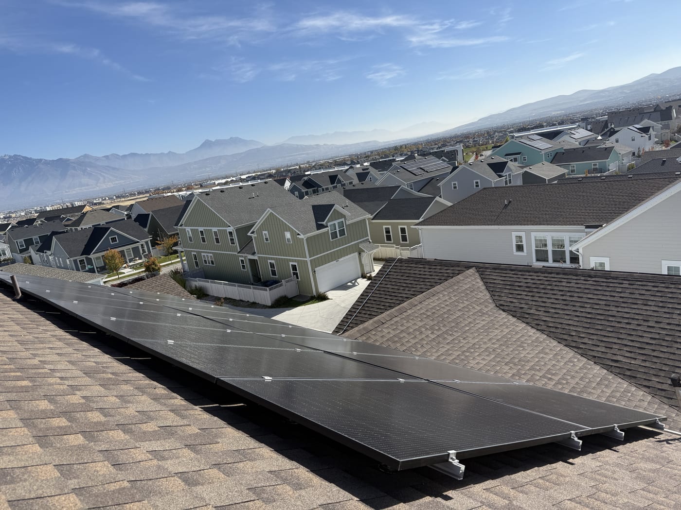 Solar panels on roof from above with suburban neighborhood and blue sky in background