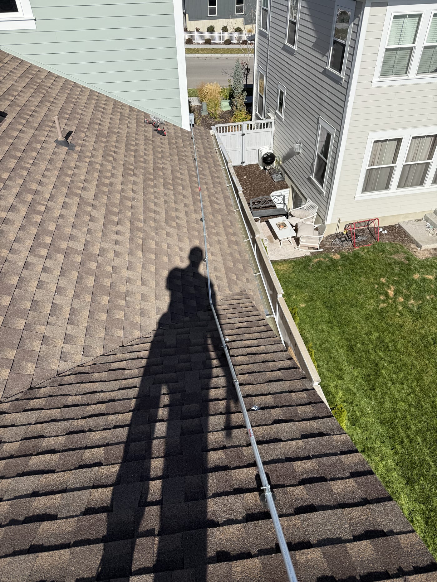 Conduit running down roof with installer shadow looking down to backyard and neighboring houses