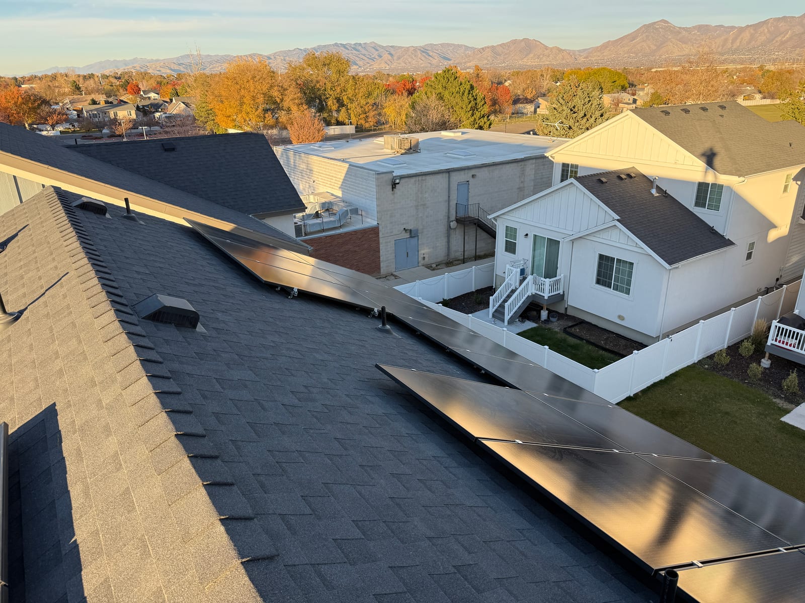 [Tier 1 Trina panels] Solar panels on multi-plane roof with Wasatch mountains and fall foliage neighborhood in background