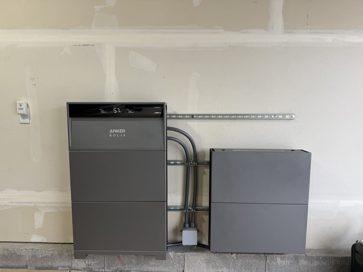 Anker Solix X1 dual battery system with conduit connections showing 51 percent on display, mounted on basement wall with concrete block visible