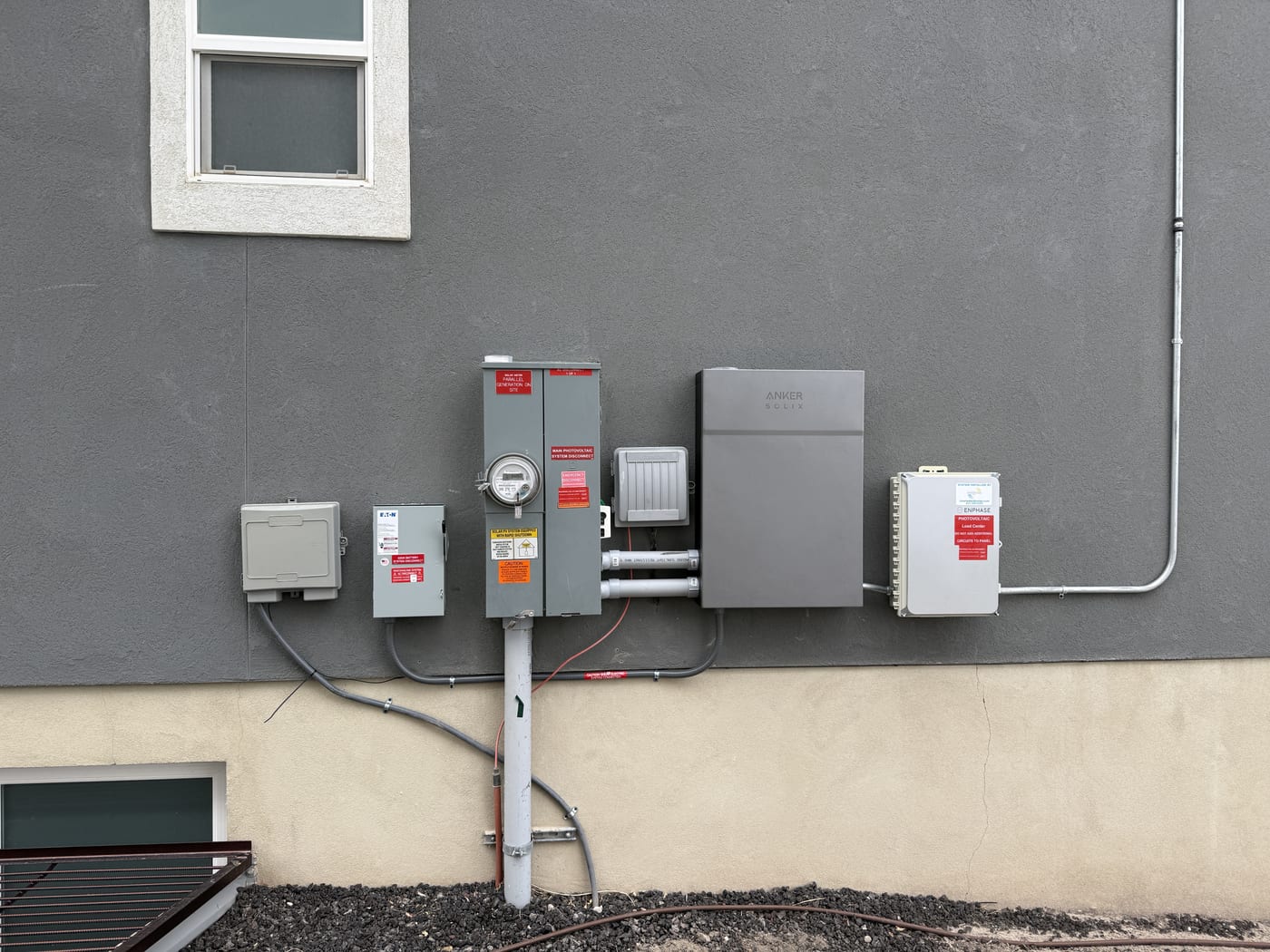 Exterior electrical equipment with disconnect meter panel and warning labels on gray stucco wall