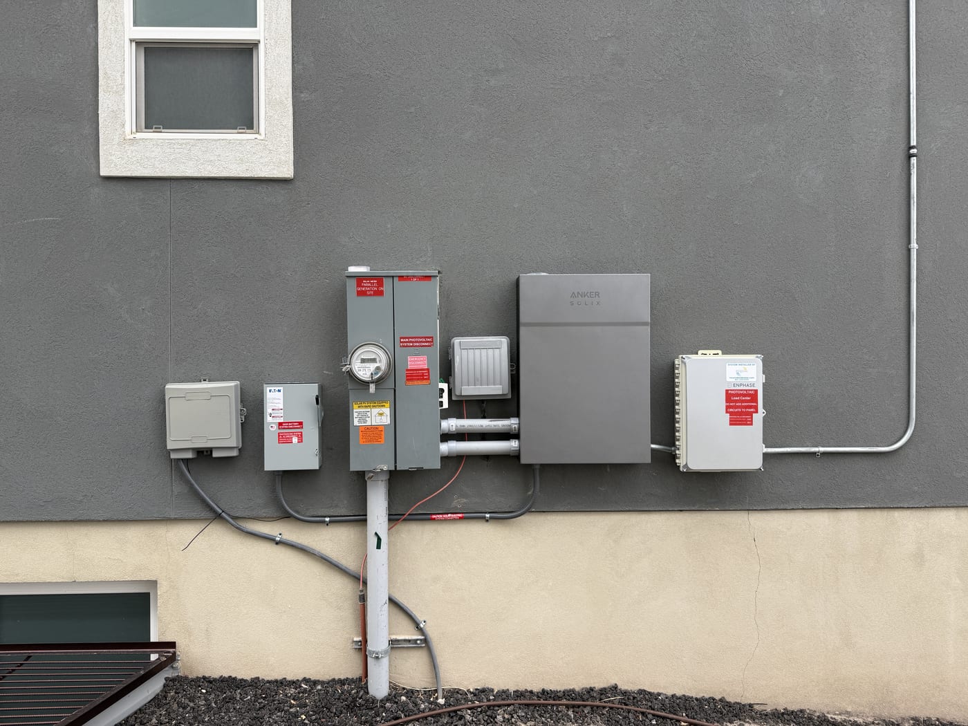 Electrical panel meter and disconnect array with conduit and labels on gray stucco exterior