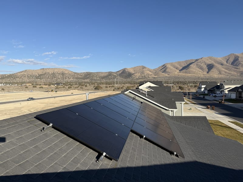 Solar panels on dark shingle roof with arid Eagle Mountain landscape and blue sky