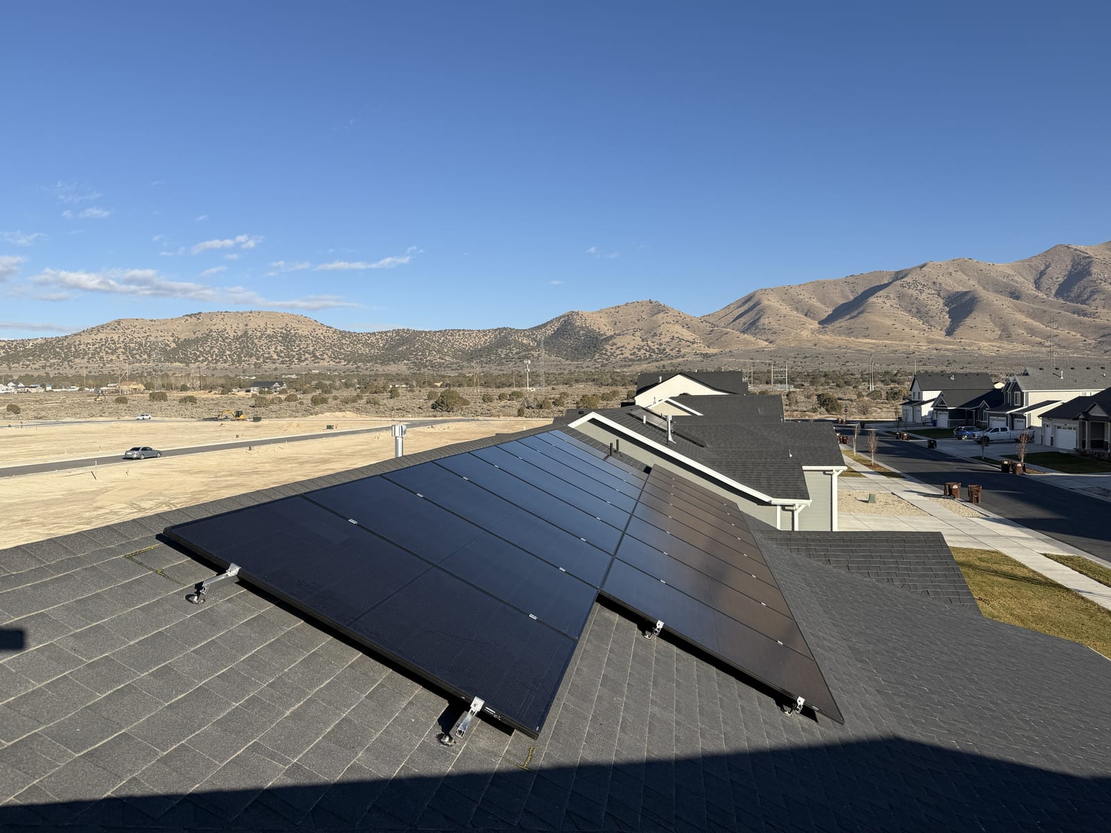 Solar panels on dark shingle roof with arid Eagle Mountain landscape and blue sky