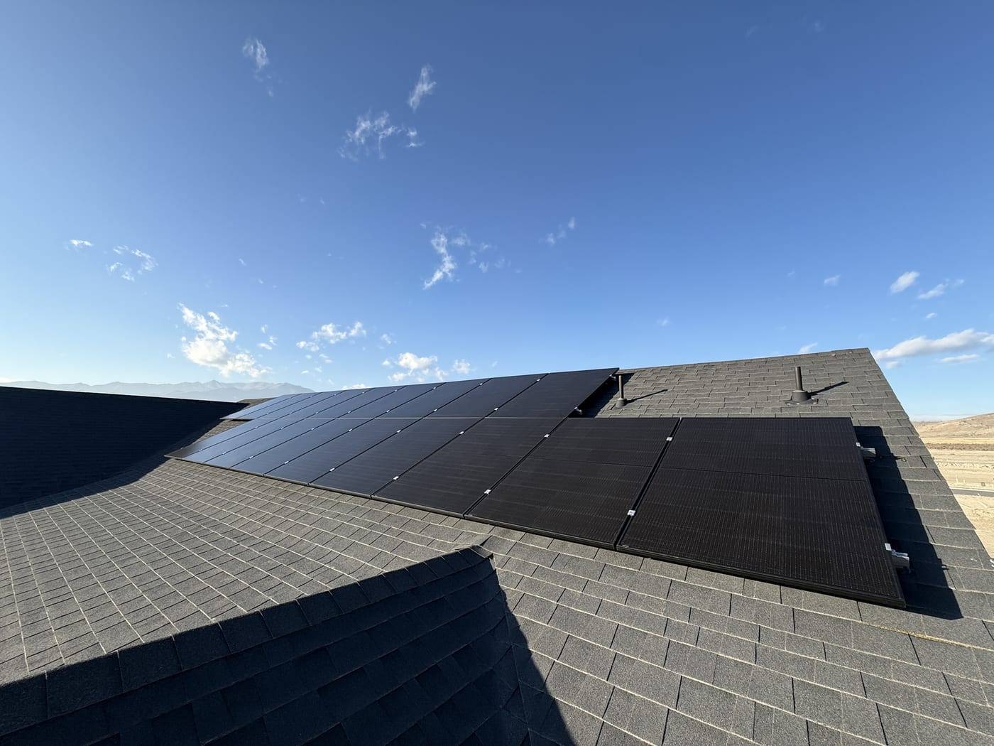 Solar panels on multi-plane dark shingle roof with blue sky and scattered clouds