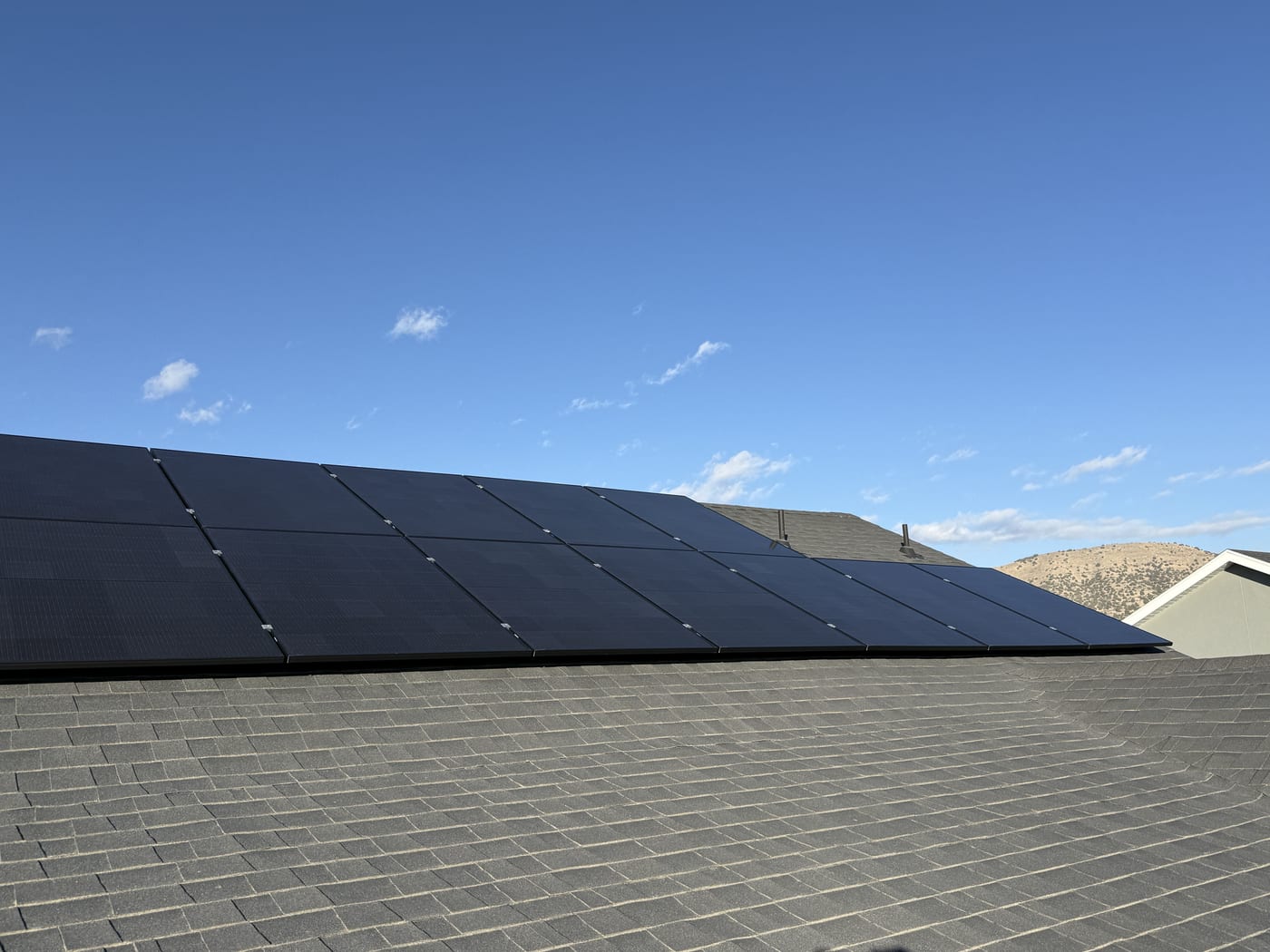 Solar panel row on dark shingle roof looking toward blue sky
