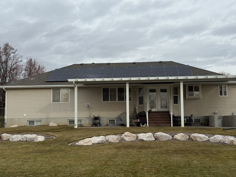 [black-on-black panels] Backyard view of house showing full solar array on roof, green lawn and porch, rotated image