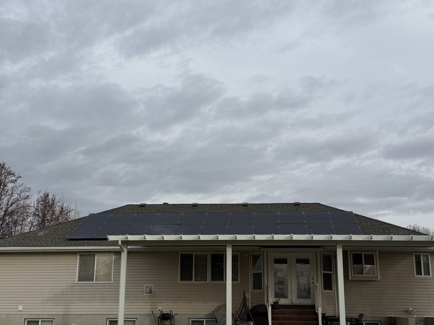 [black-on-black panels] Front view of house with solar panels visible on roof, rotated image, overcast sky