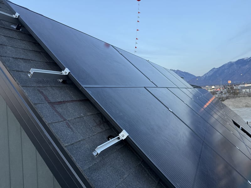[Tier 1 Trina 410W black-on-black panels] Close-up of installed black solar panels with clamps on racking, snow-capped mountains in background