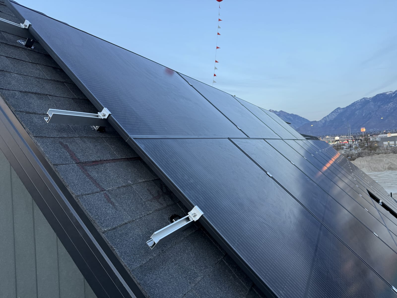 [Tier 1 Trina 410W black-on-black panels] Close-up of installed black solar panels with clamps on racking, snow-capped mountains in background