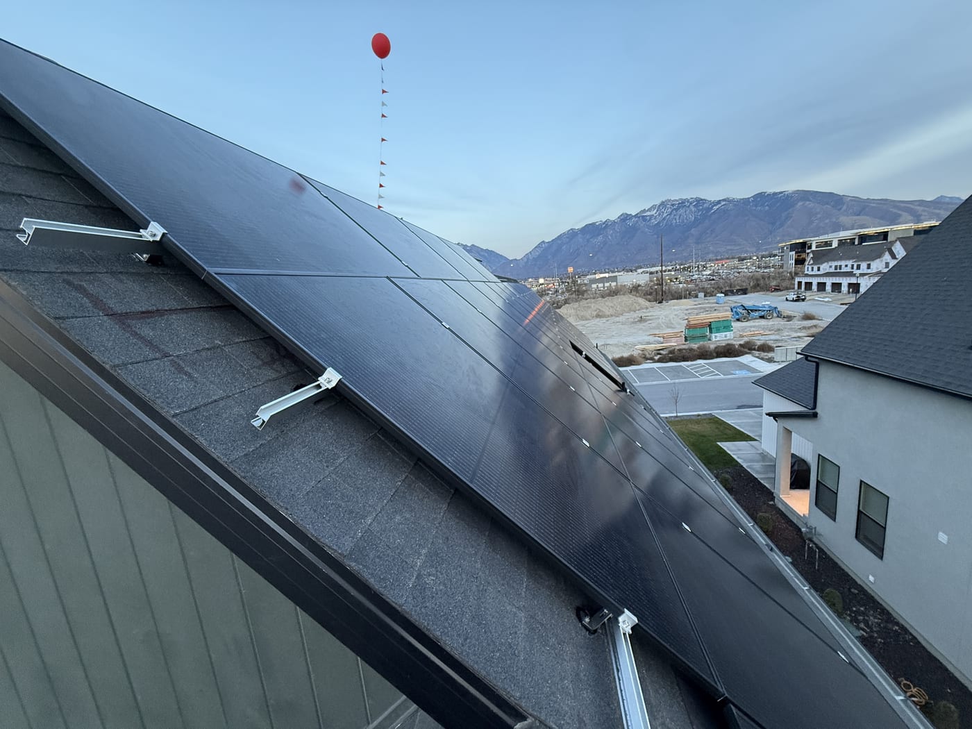 [Tier 1 Trina 410W black-on-black panels] Row of black solar panels on roof looking toward mountains and neighborhood, clear sky