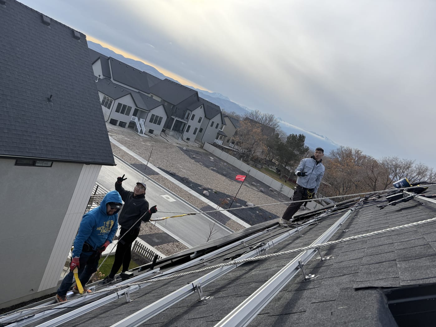 [Tier 1 Trina 410W black-on-black panels] Two crew members installing solar panels at sunset, warm light on panels and racking