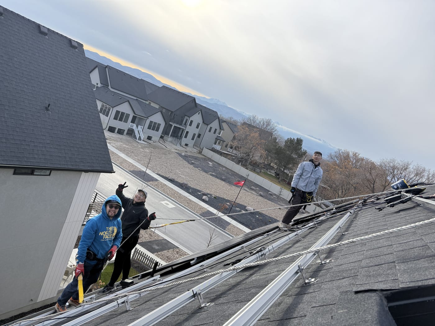 [Tier 1 Trina 410W black-on-black panels] Crew handling solar panel on racking at sunset, close perspective from roof showing neighborhood below
