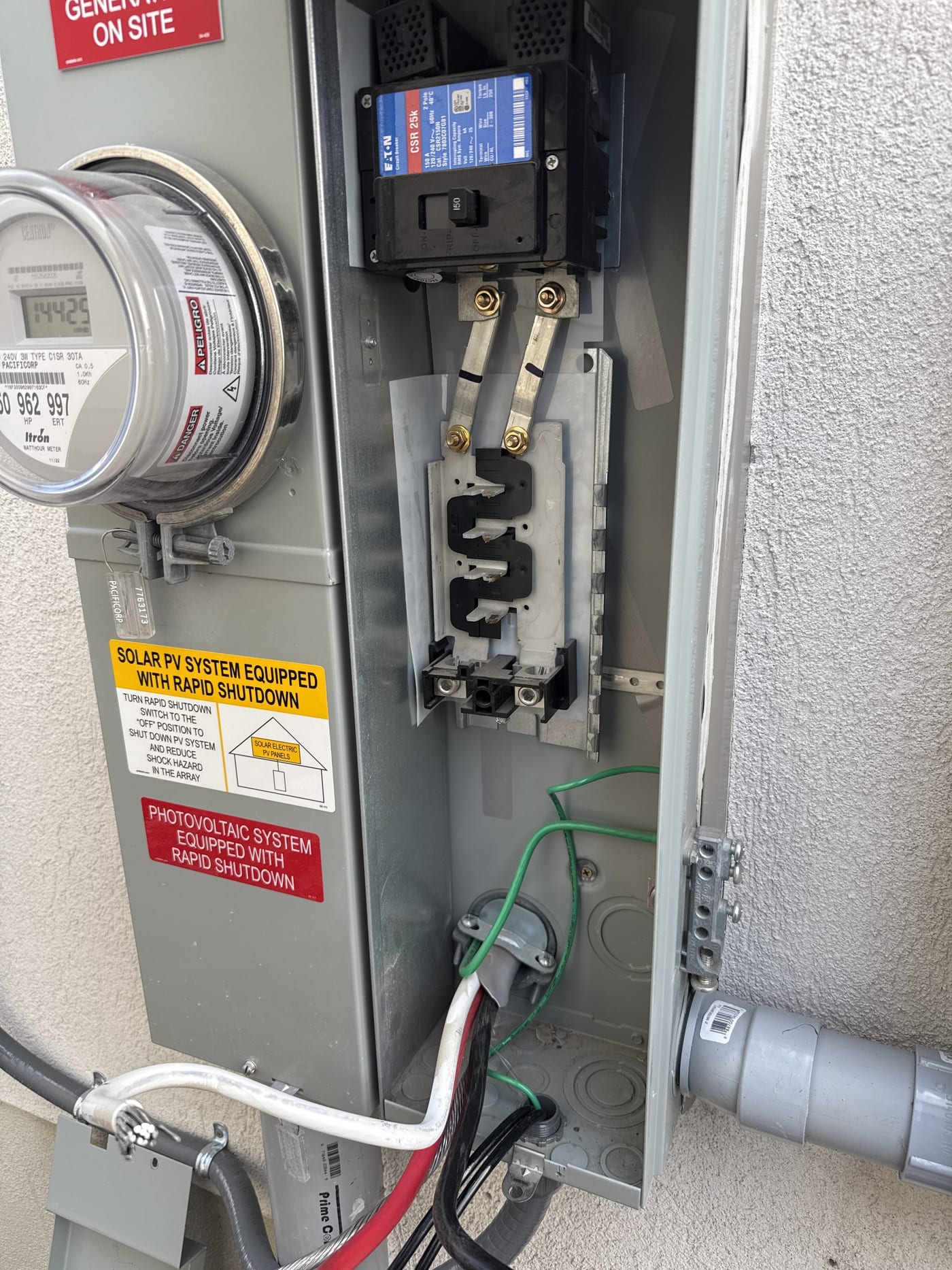 Electrical meter panel with rapid shutdown sticker, disconnect switch, and conduit connections on house exterior