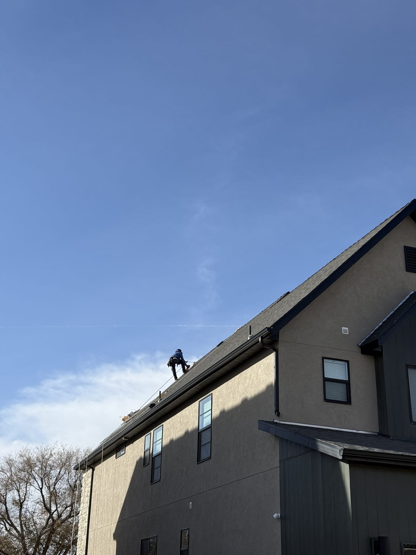 Ground-level view of house exterior with crew member on roof ridge, mountains and new construction neighborhood in background
