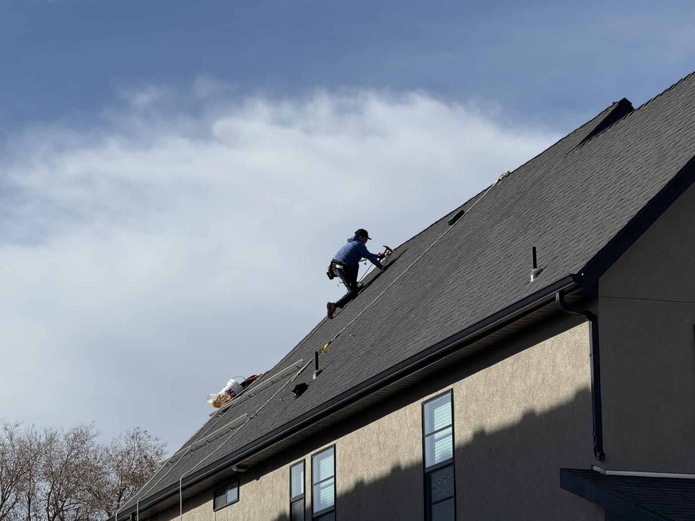 Wider view of house with crew on roof, mountains and subdivision visible in background