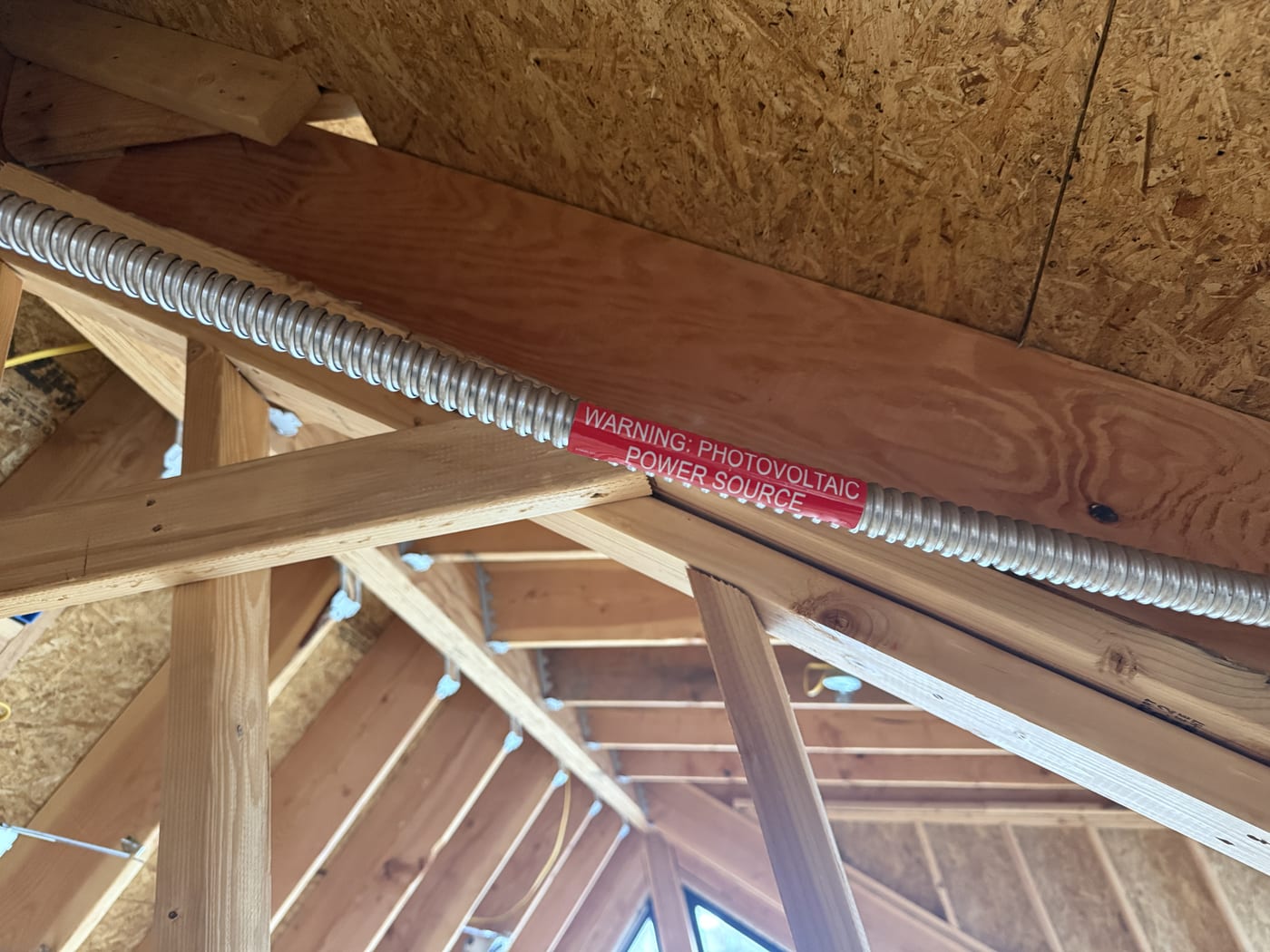 Solar conduit and wiring run through open ceiling joists in new construction framing, junction box visible