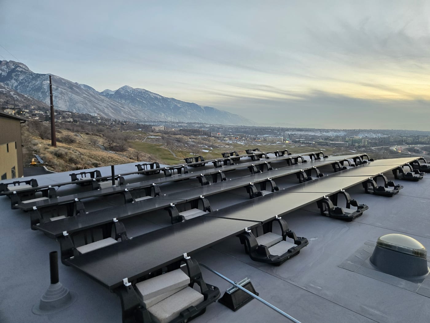 Ballasted solar array on flat roof with panoramic Wasatch mountain view, overcast sky with golden horizon