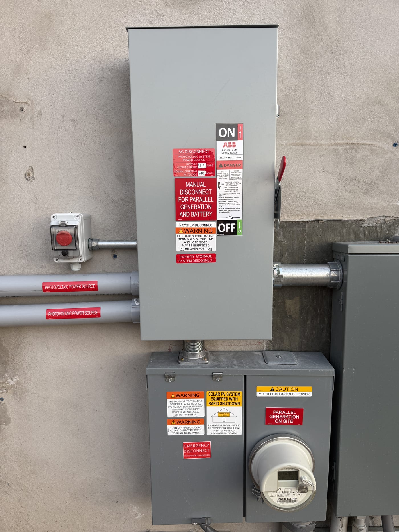 Exterior electrical panel with ABB disconnect switch, meter socket, rapid shutdown button, and warning labels on concrete wall