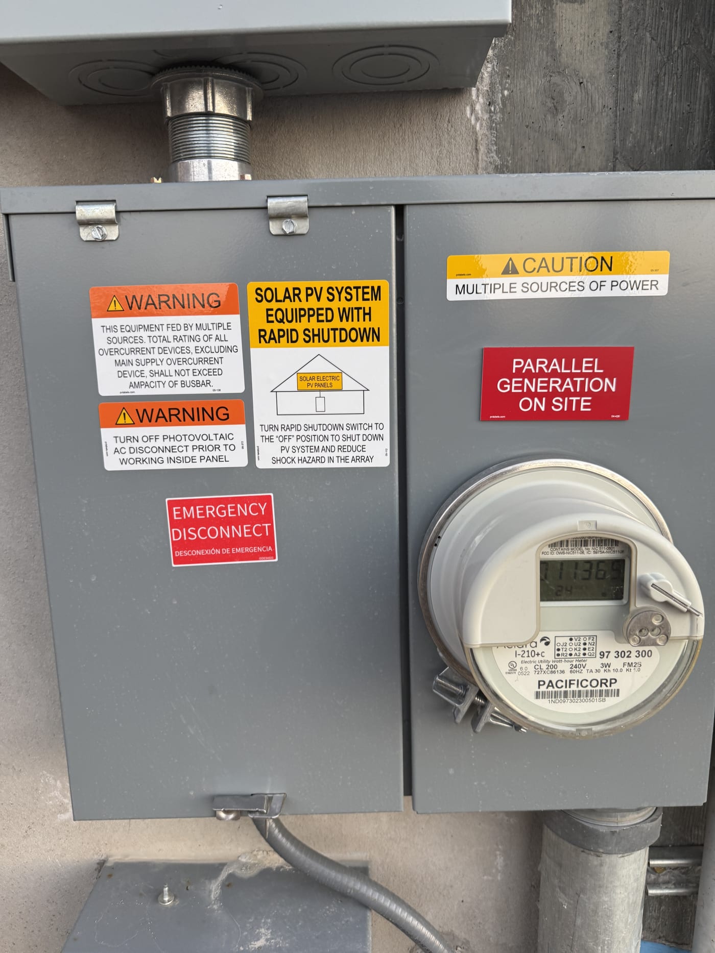 Close-up of PacifiCorp meter with rapid shutdown and parallel generation warning stickers, emergency disconnect label