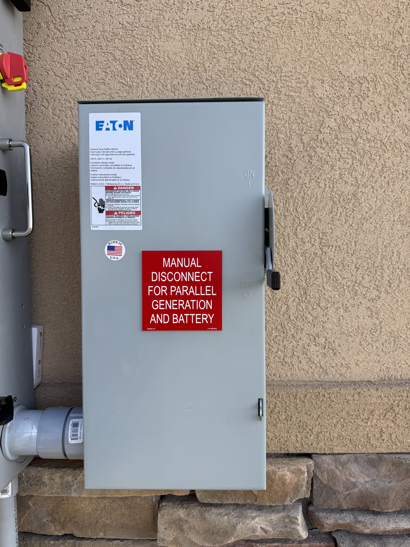 Eaton manual disconnect switch for parallel generation and battery with red warning label, mounted on exterior stucco wall