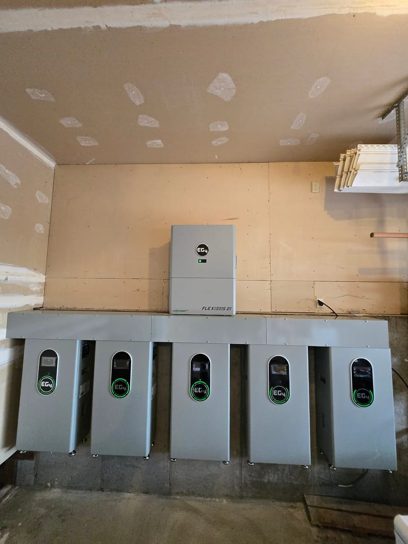 Massive EG4 battery wall with FlexBOSS 21 inverter and five EG4 batteries on plywood backboard in garage, all units powered with green LEDs