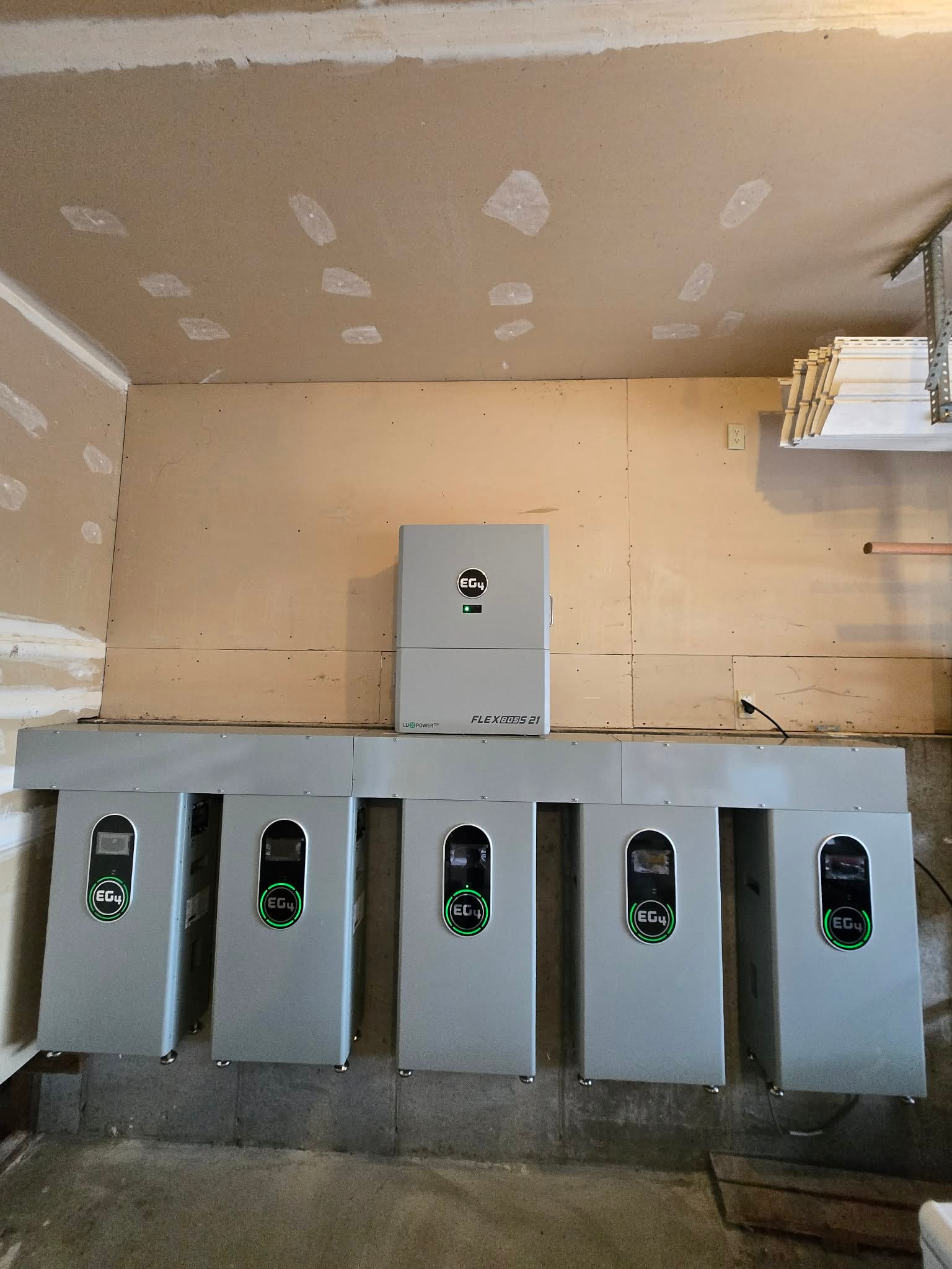 Massive EG4 battery wall with FlexBOSS 21 inverter and five EG4 batteries on plywood backboard in garage, all units powered with green LEDs