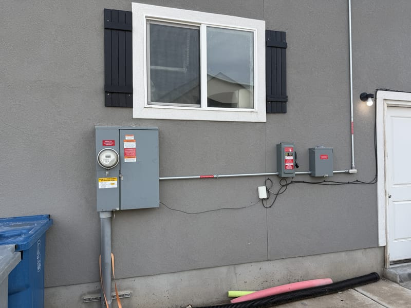 Exterior wall of gray stucco home showing solar disconnect box, electrical meter and panel, with conduit runs and wiring between components (image rotated sideways)